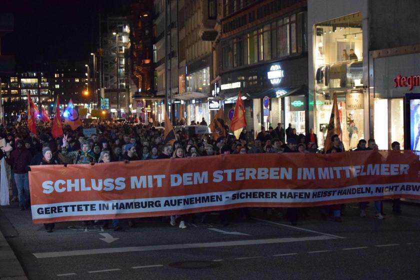 Almanya'nın Hamburg kentinde düzenlenen mültecilerle dayanışma mitinginde 'Schluss mit dem sterben im mittelmeer' yazılı pankartın arkasında yürüyen kalabalık.