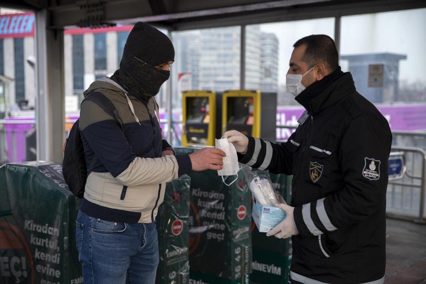 Maske dağıtan güvenlik görevlisi (sağda) ve maskeyi alan bir yolcu