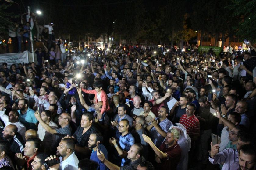 Eylem yapan öğretmenler, hava kapalı, öğretmenler ellerinde telefon ışığı ile kadrajın sol tarafına bakıyor