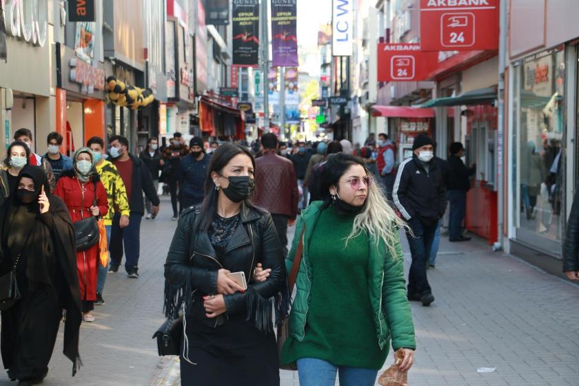 Önde iki genç kadın kol kola girmiş yürüyor, birinde maske var diğeri maskesini çenesine indirmiş