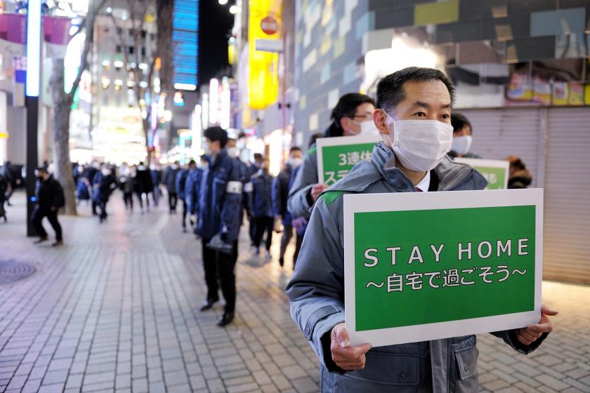 Tokyo'da elinde evde kal yazan bir döviz taşıyan erkek