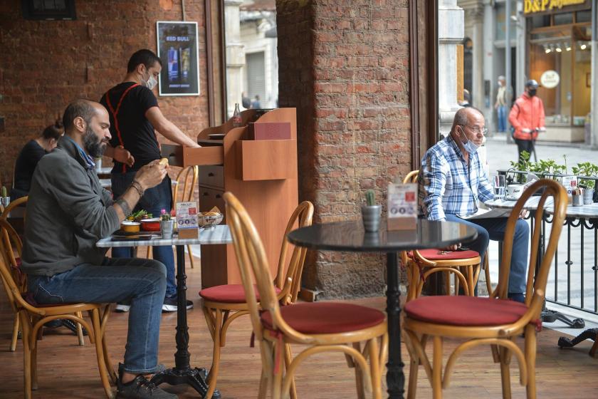 Bir restoranda iki masada oturan müşteriler, ayakta bir çalışan