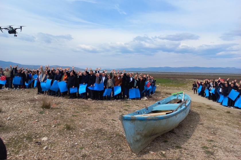 Marmara Gölü'nün kuruyan bölümünde ellerinde mavi karton olan kişiler. 