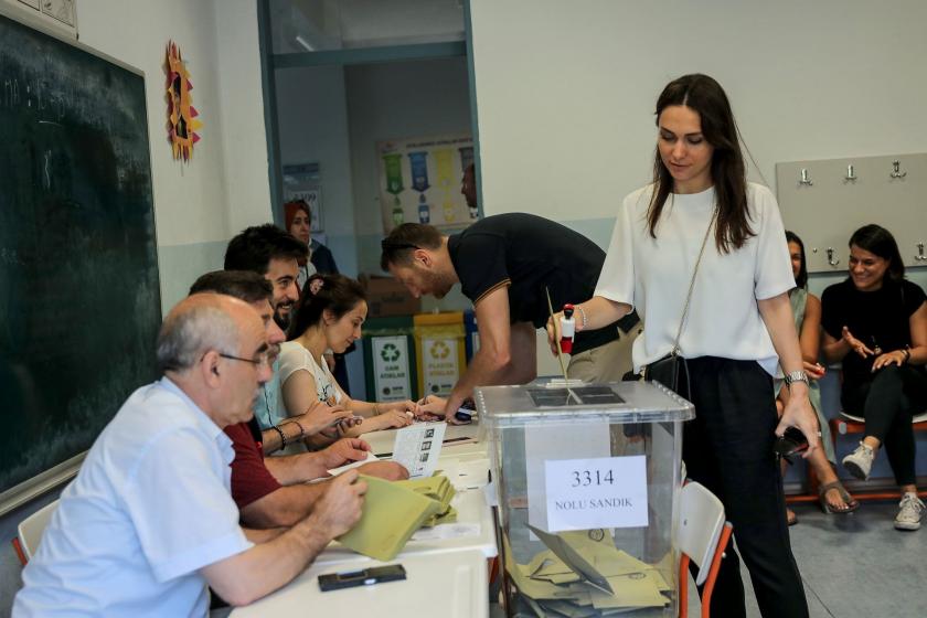 sandık kurulu önünde oy sandığı ve oyunu atmakta olan genç bir kadın