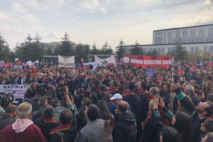 Yüzlerce avukat cübbeleriyle alanda basın açıklamasını dinliyor. Avukatların arasından yükselen kırmızı fonlu 