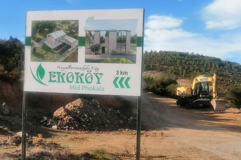 Foça yakınlarındaki ekoköy projesinin beyaz, üzerinde ekoköy projesine ilişkin fotoğraflar bulunan tabelası.