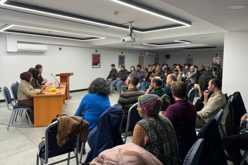 kürsüde konuşan 3 kişi ve salonda dinleye insanlar