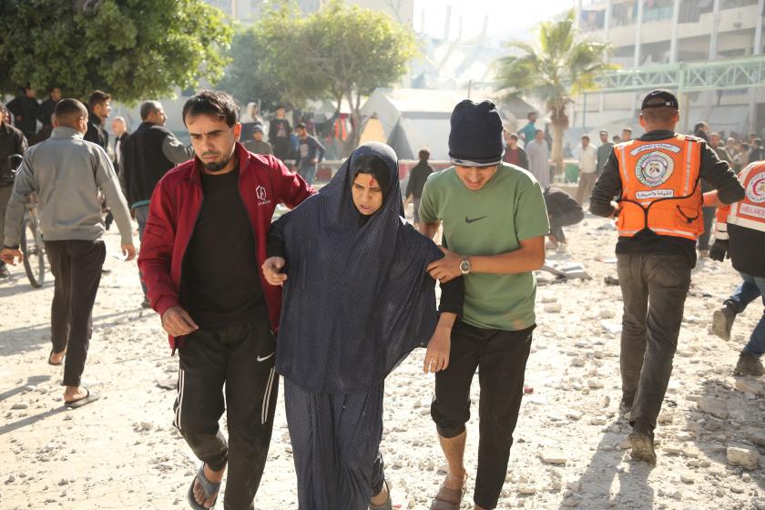 sladırı sonrası yaralanan bir kadının koluna giren iki erkek, arkada moloz yığınları ve kalabalık