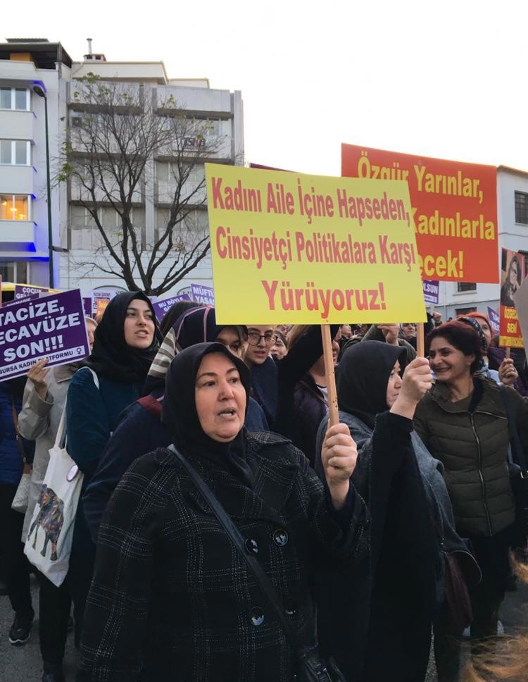 Elinde 'Kadını aile içine hapseden cinsiyetçi politikalara karşı yürüyoruz!' yazılı döviz tutan başörtülü bir kadın