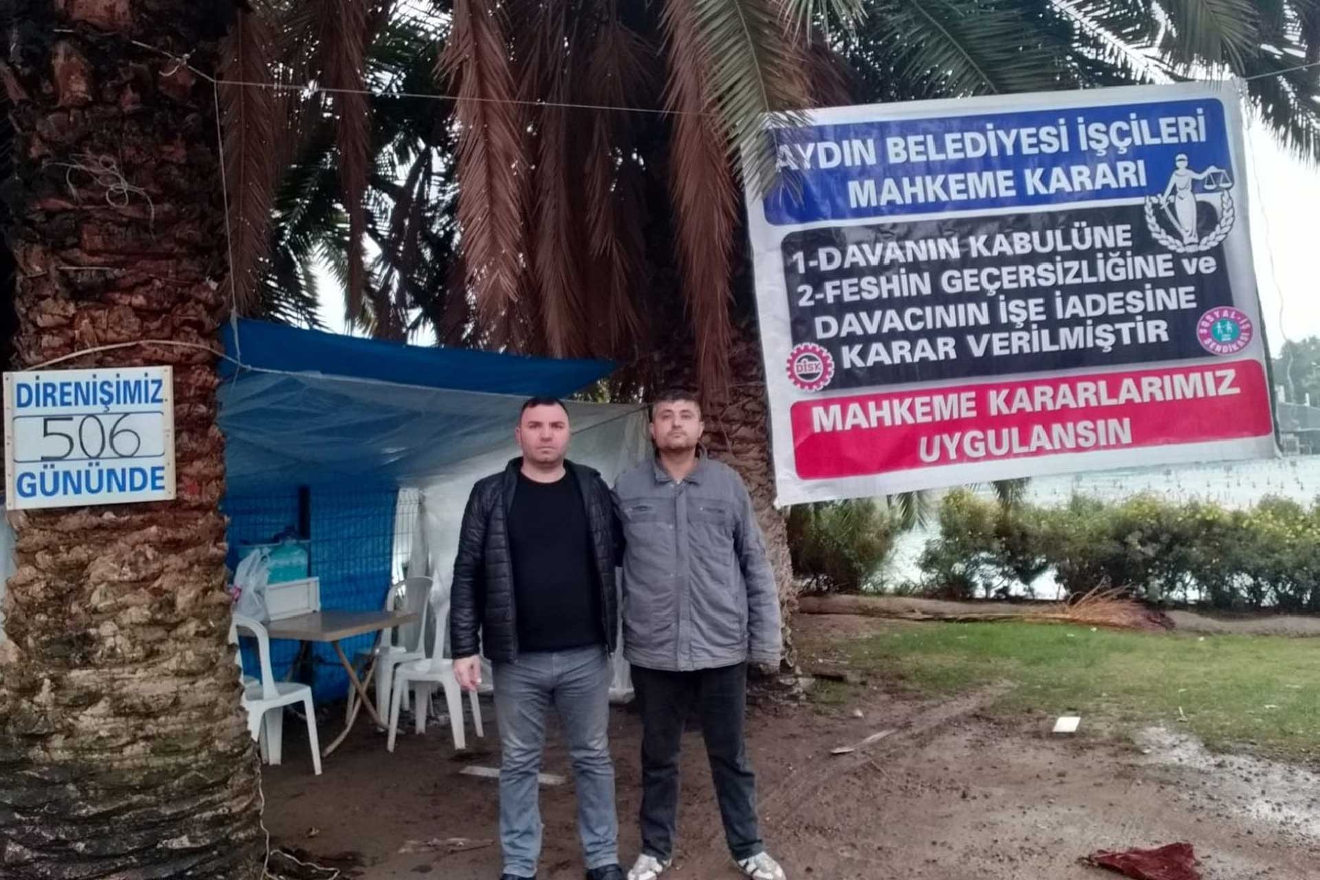 2 Aydın Belediyesi işçisi direniş çadırının önünde poz veriyor