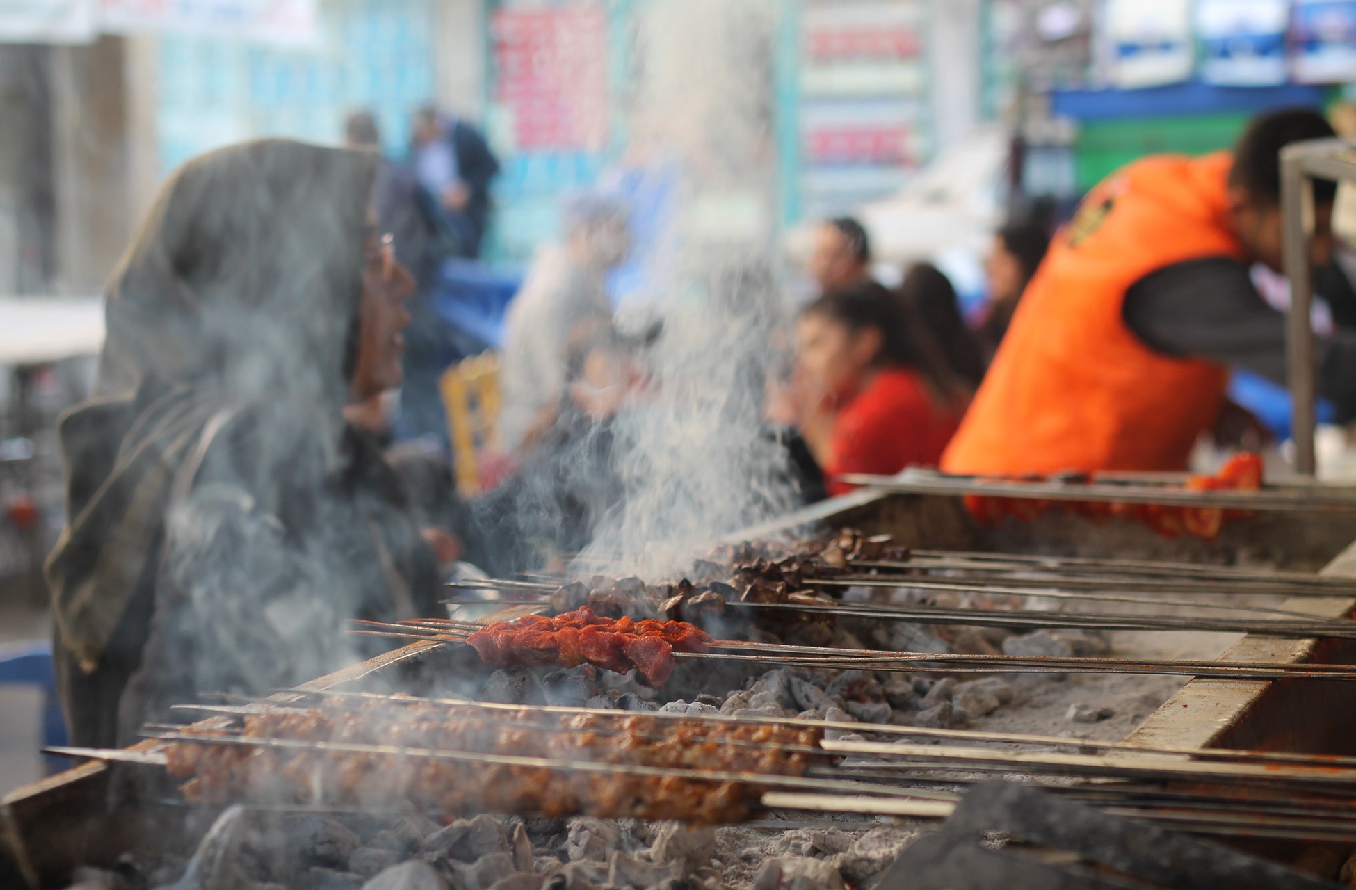 Kebapçıda mangal üzerinde pişen kebaplar ve müşteriler.