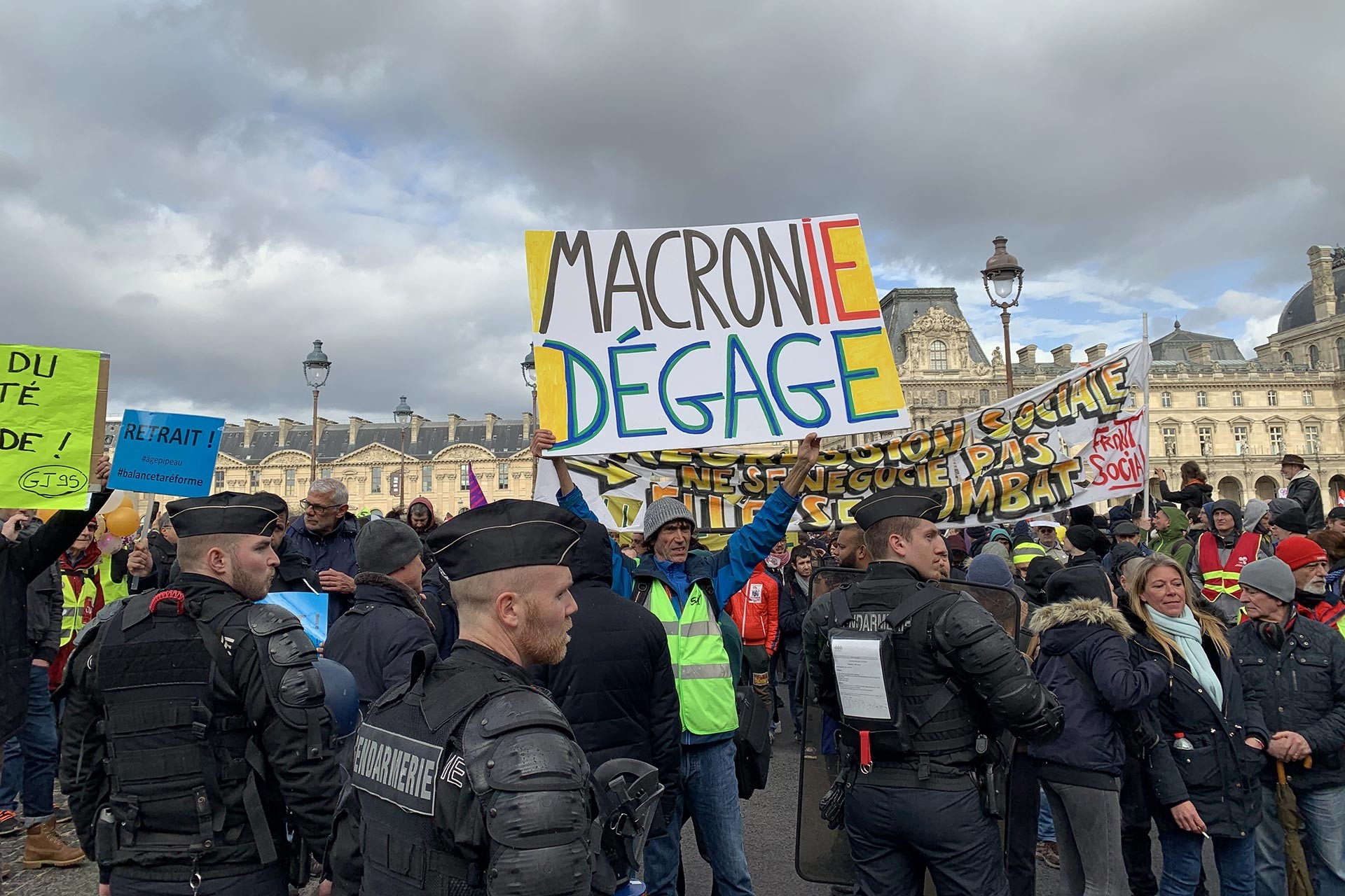 Macron istifa yazılı bir döviz taşıyan kişi ve çok sayıda eylemci ve polisler.