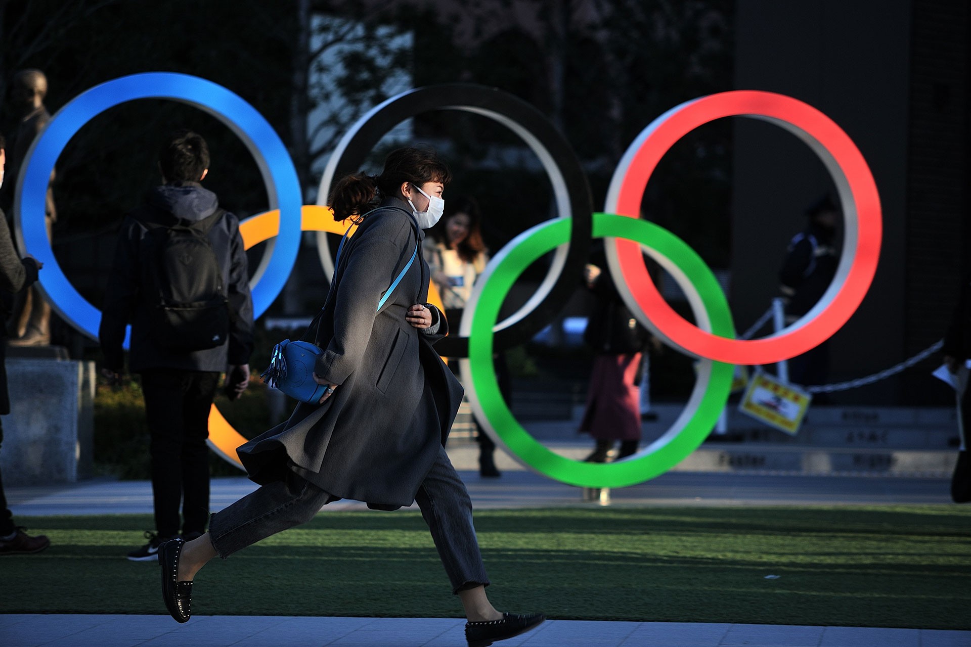 Tokyo'da sokakta yürüyen bir kadın ve olimpiyat heykeli