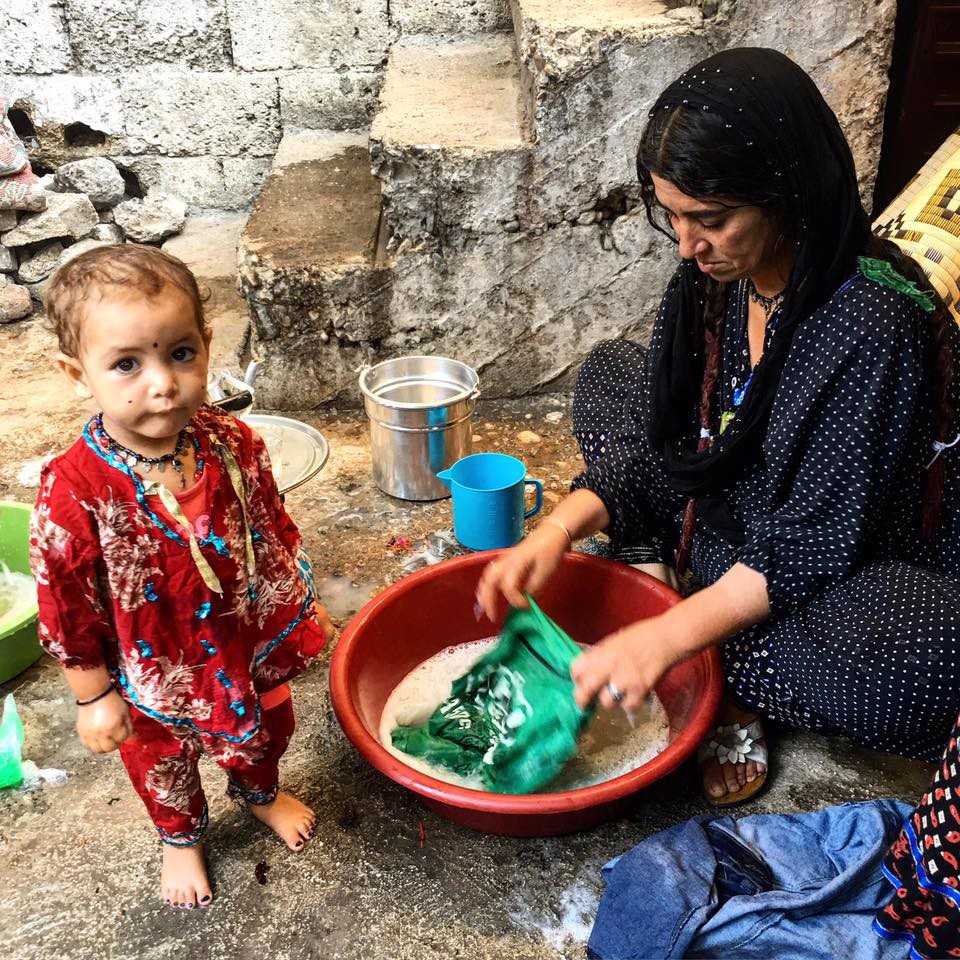 Romen bir anne leğende çamaşır yıkıyor. Yanında bir çocuk. 