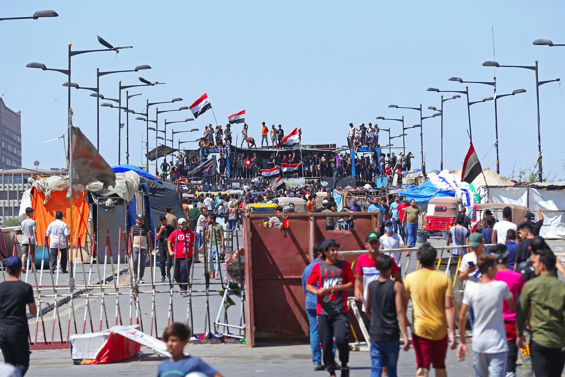 Irak'ta sokağa çıkan yüzlerce kişi, sağ tarafta gençler yan yana yürüyor, önlerinde barikat var