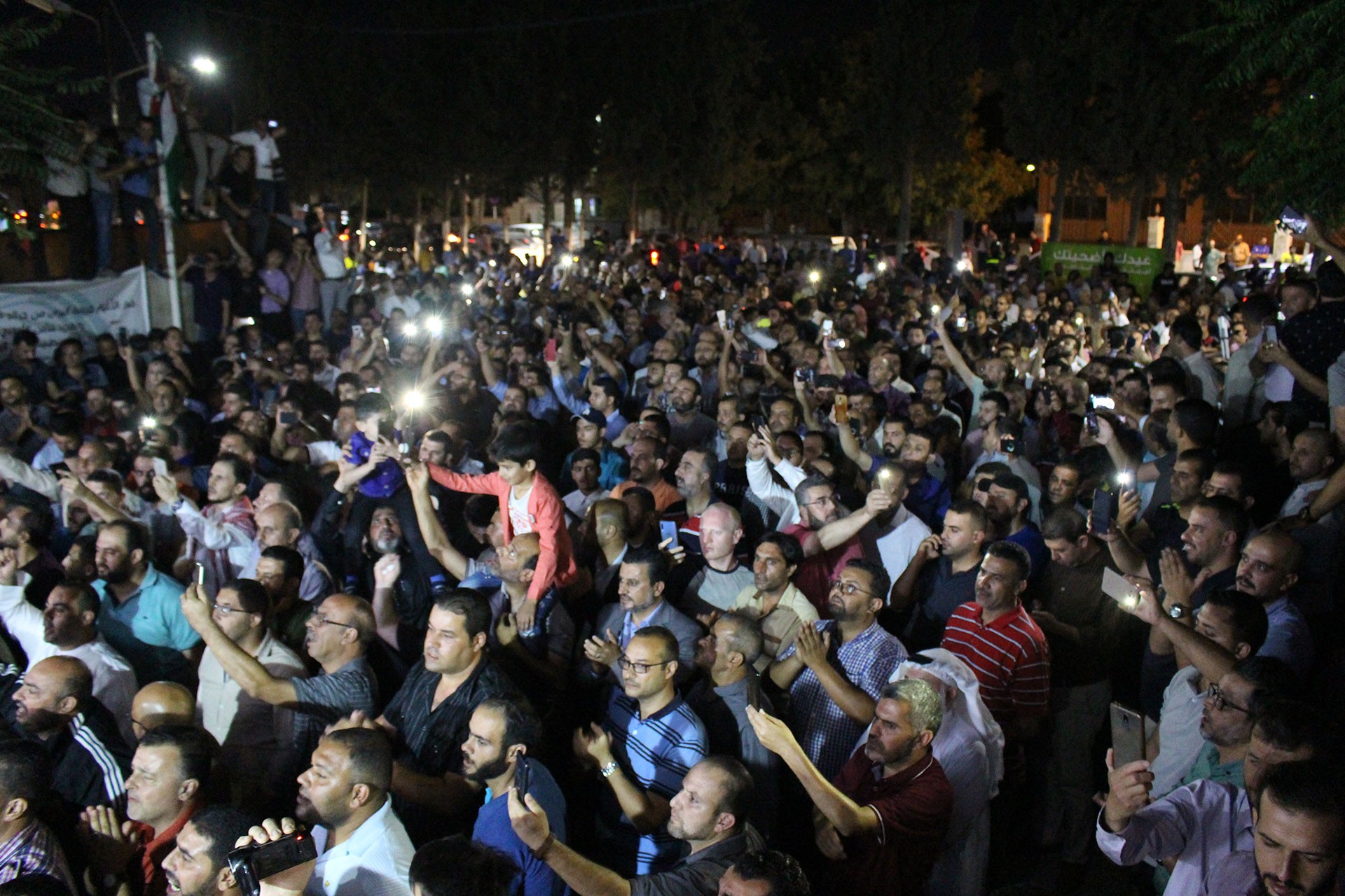 Eylem yapan öğretmenler, hava kapalı, öğretmenler ellerinde telefon ışığı ile kadrajın sol tarafına bakıyor