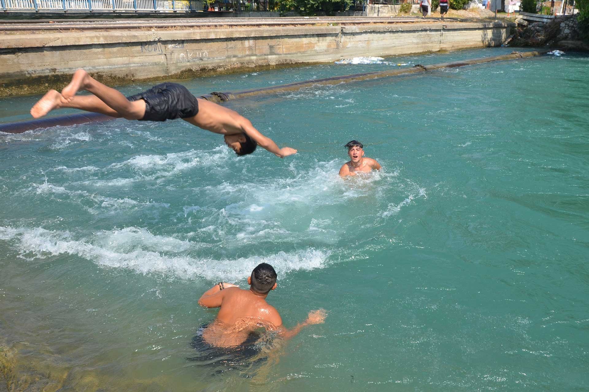 Adana'da su kanalında serinlemeye çalışan gençler