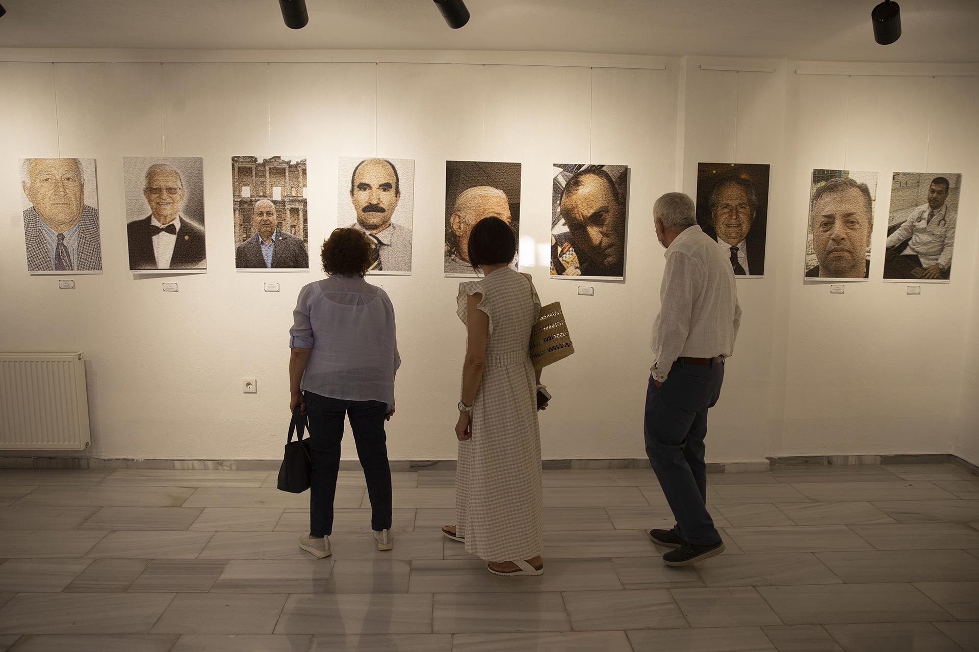 Fotoğraf sergisi, duvarda sağlık çalışanlarının portreleri ve onlara bakan 3 kişi