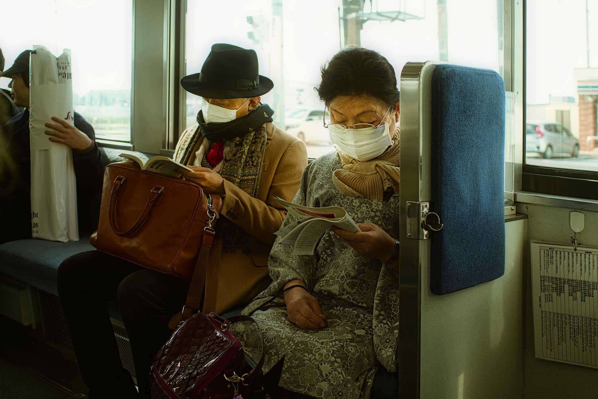 Tramvayda oturan Japon erkek kitap okuyor (solda) kadın gazete okuyor (sağda) 