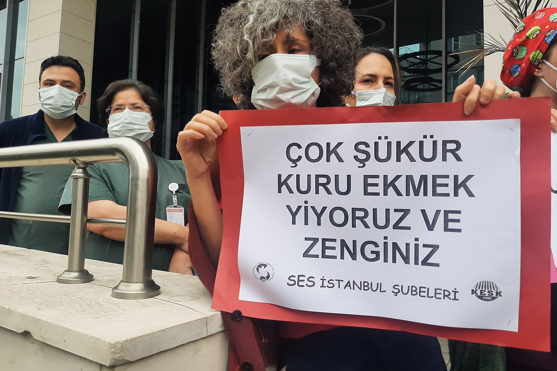 Sağlık emekçilerinin gerçekleştirdiği eylemde 'Çok şükü kuru ekmek yiyoruz ve zenginiz' yazılı döviz tutan bir sağlık emekçisi.