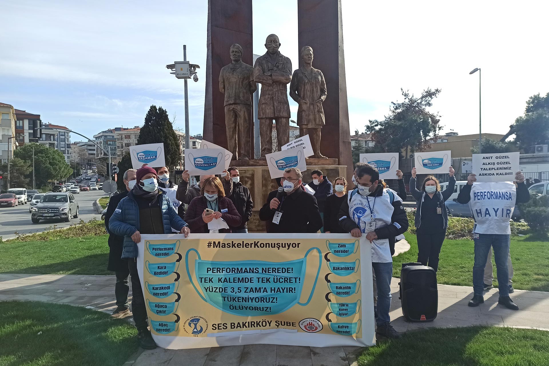 Sağlık emekçileri sağlıkçılar için dikilen heykelin önünde, taleplerini içeren pankartlarıyla.