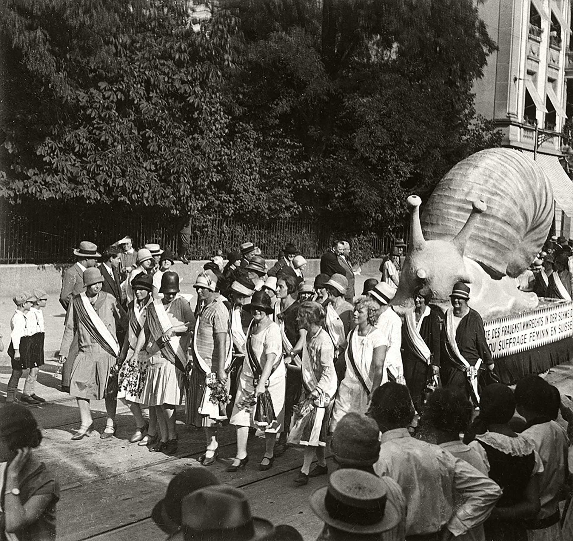 1928 yazında İsviçreli Kadın İşleri Sergisi kortejinde bir kağnı arabasının üzerine, taleplerinin karşılanma hızını simgeleyen salyangoz şeklinde dev bir maket konur, üzerine de 'Kadınların Oy Hakkı' yazılır