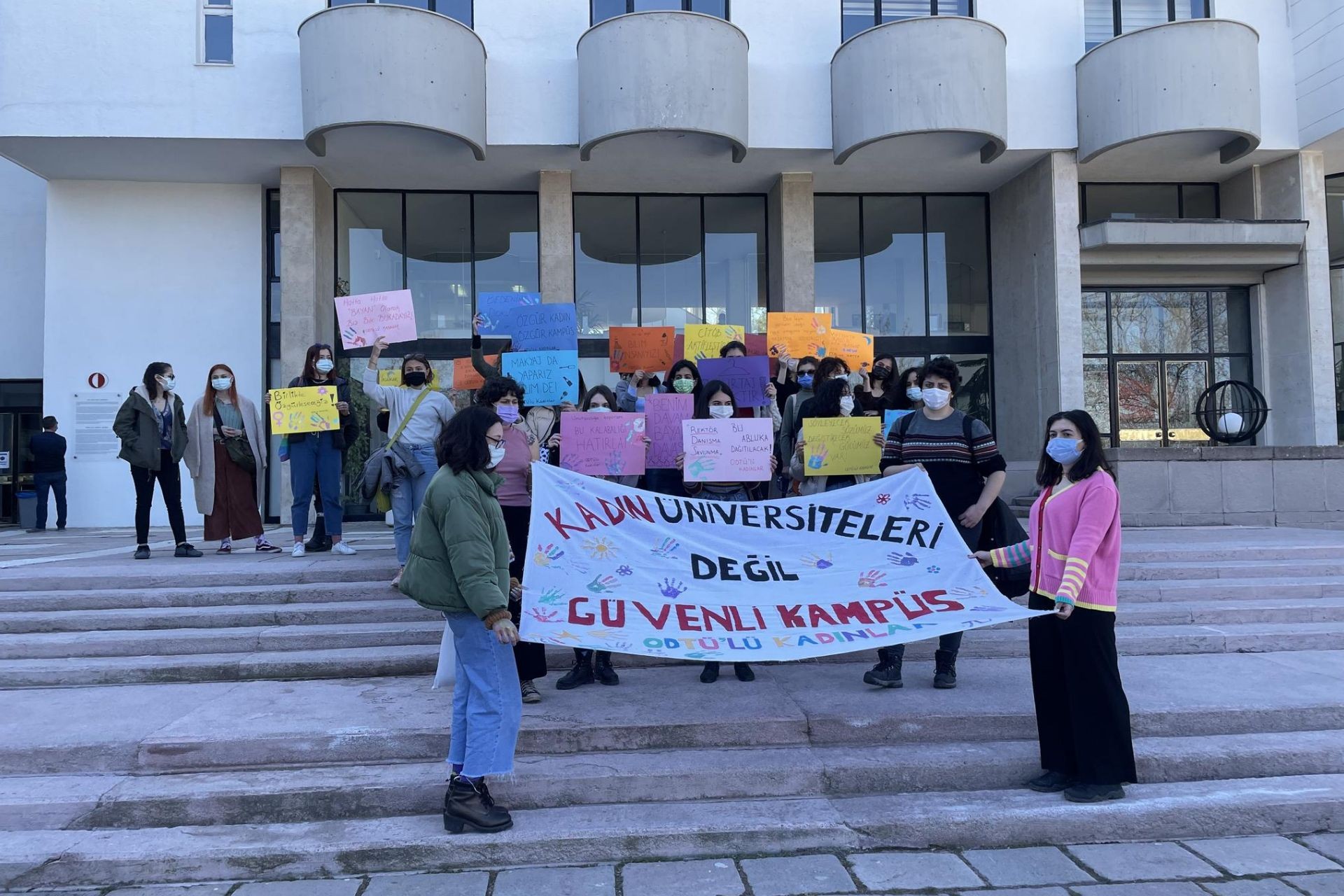 Kadın üniversiteleri değil güvenli kampüs yazan pankartın arkasında toplanan kadınlar