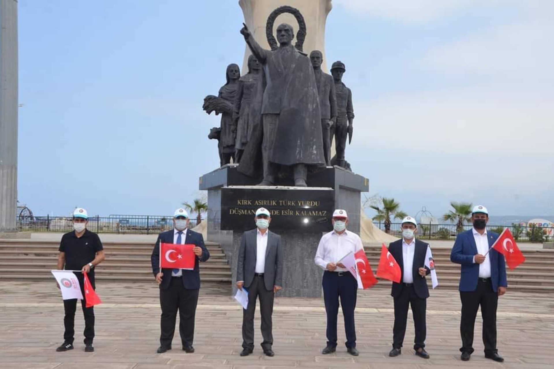 Altı Hak-İş yöneticisi ellerinde bayrak heykelin önünde 1 Mayıs kutluyor