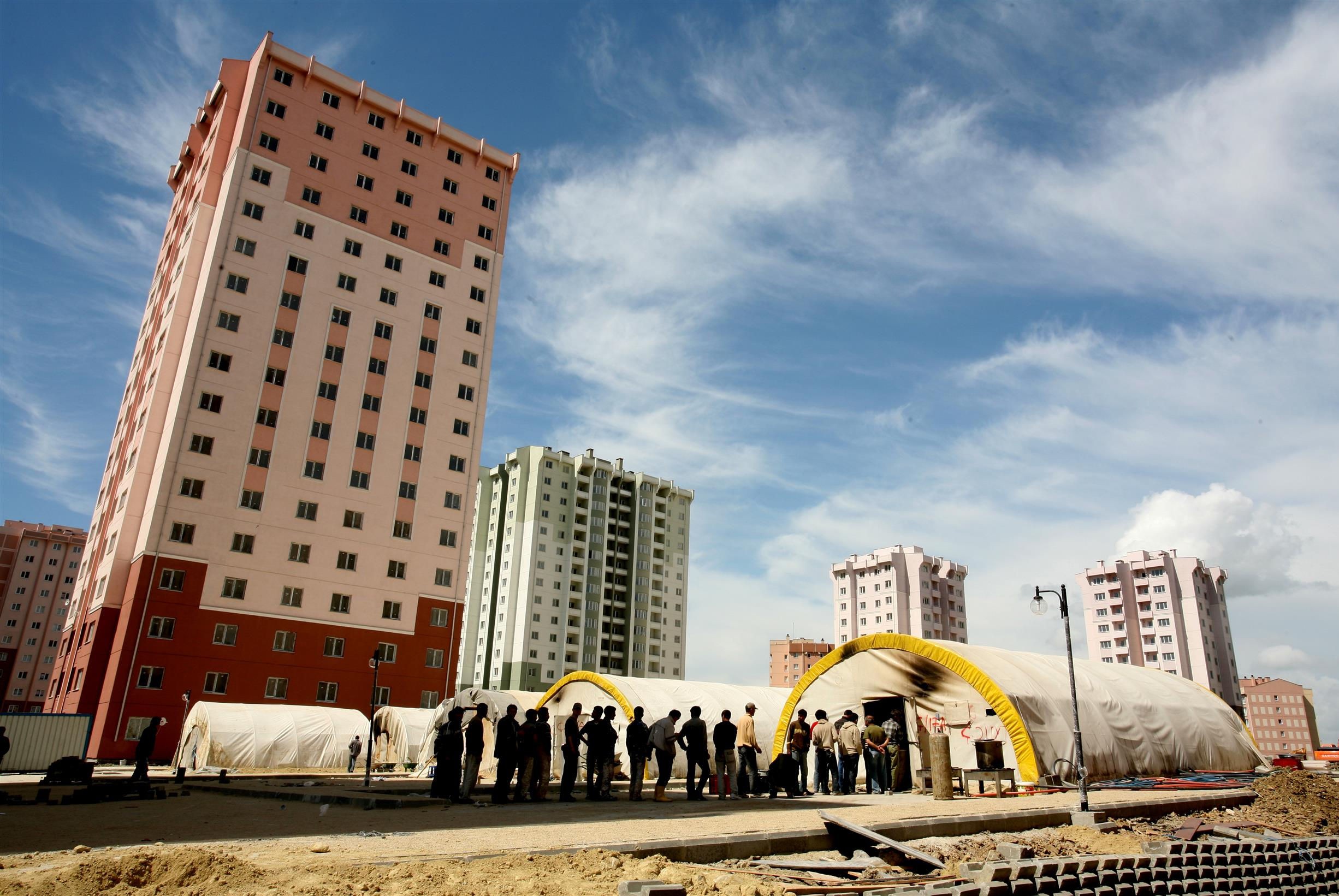 Yeni yapılmış çok katlı apartmanların önünde çadırlar ve insanlar