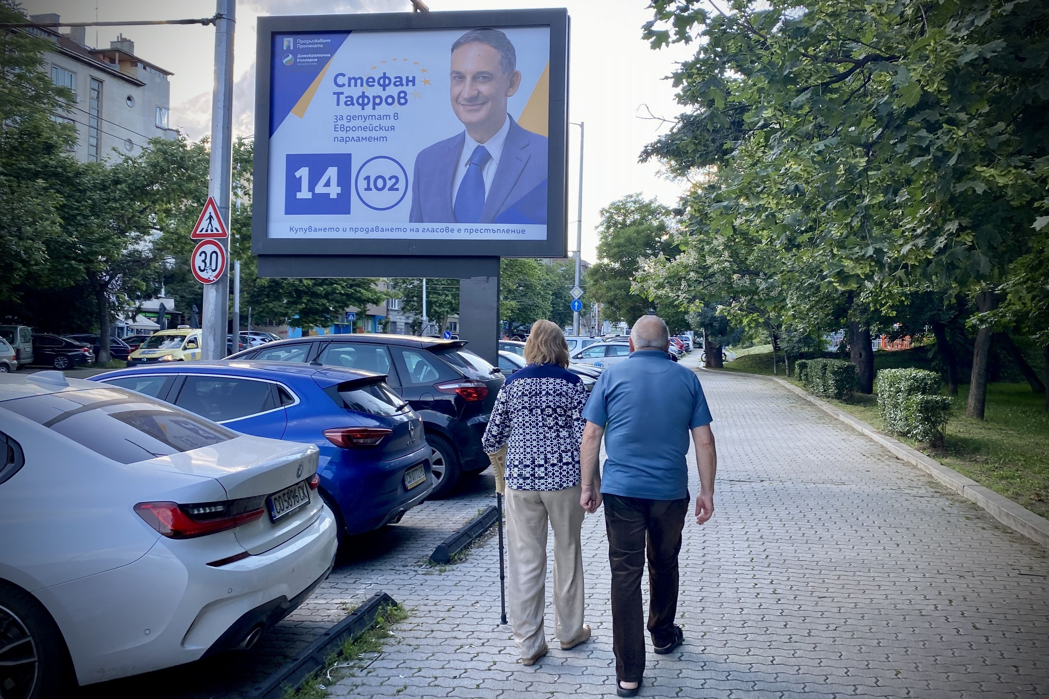 Bulgaristan'da AP adayının tanıtım afişi ve sokakta yürüyen iki insan