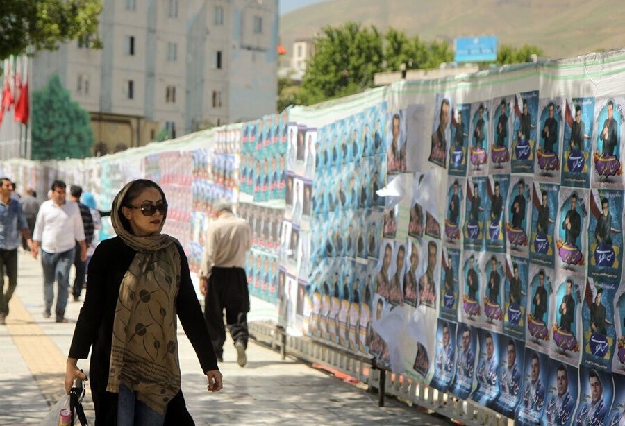 İran'da seçim afişlerinin önünde yürüyen kadın.