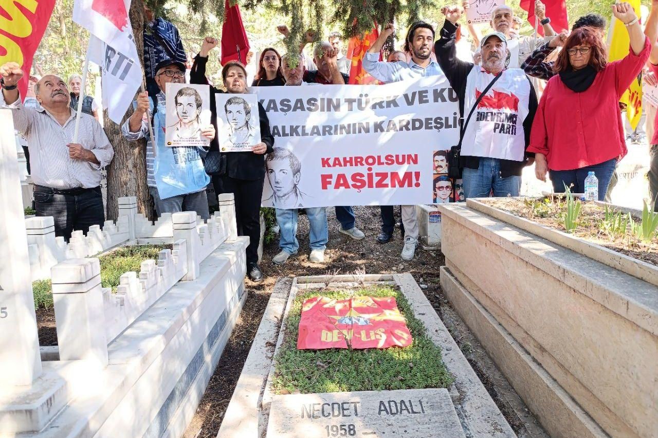 mezar başında pankart ve bayrak tutan insanlar