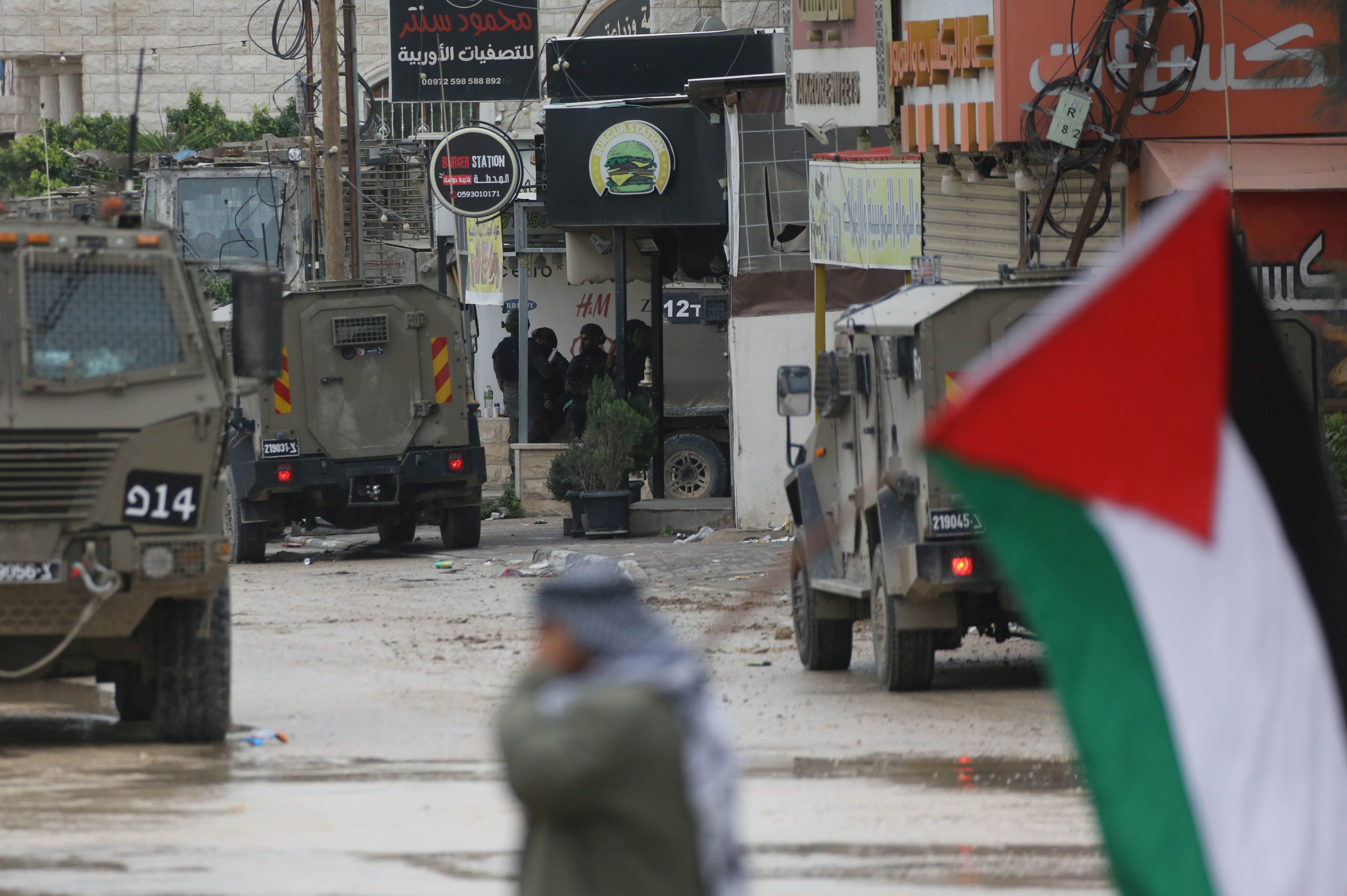 Flistin bayrağı taşıyan bir kişi, israil askerleri, zırhlı araçlar